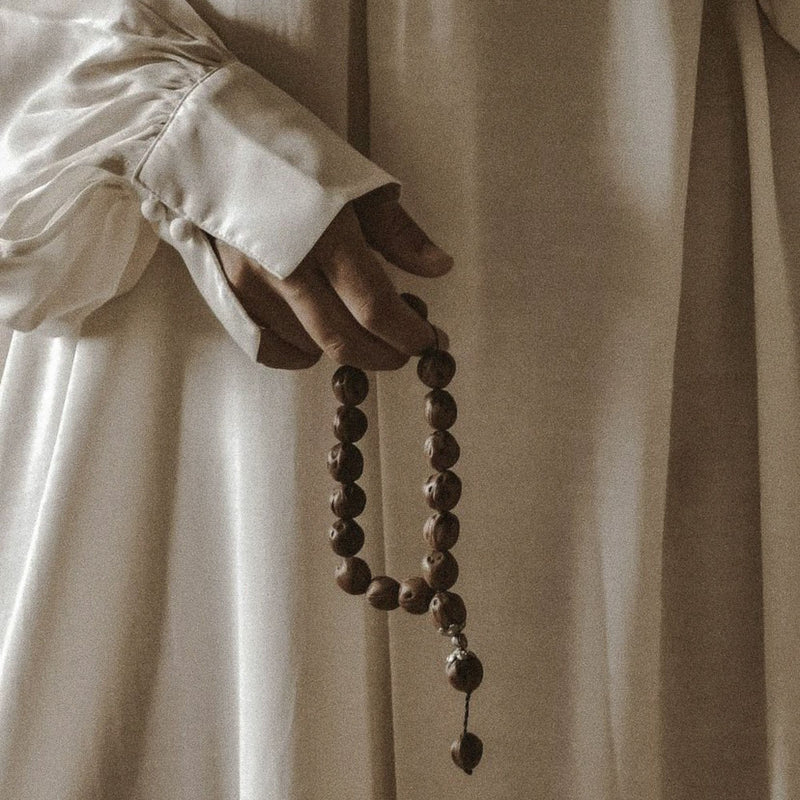 Femme en robe blanche tenant un tasbih dans la main