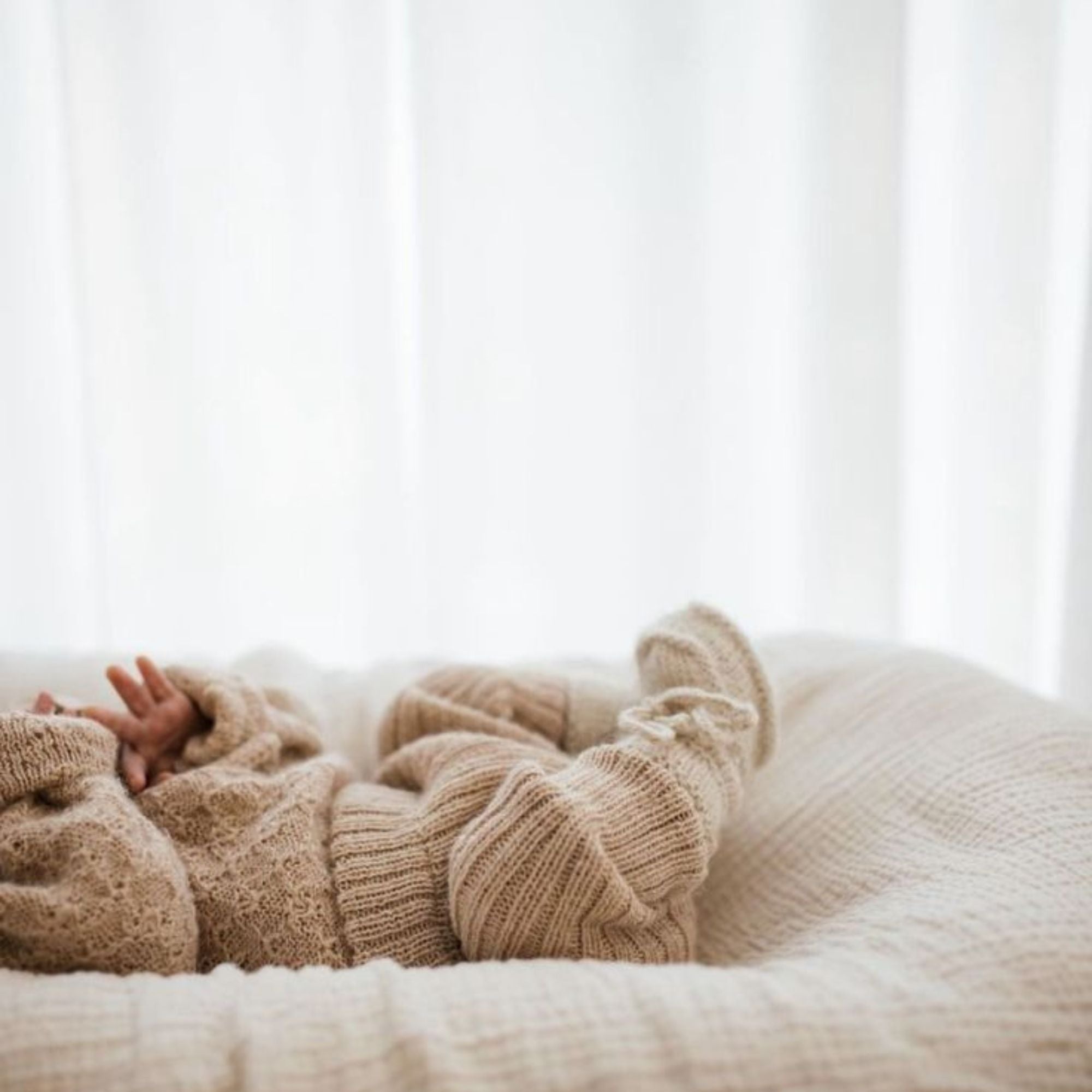Bébé dans un vêtement en laine beige allongé